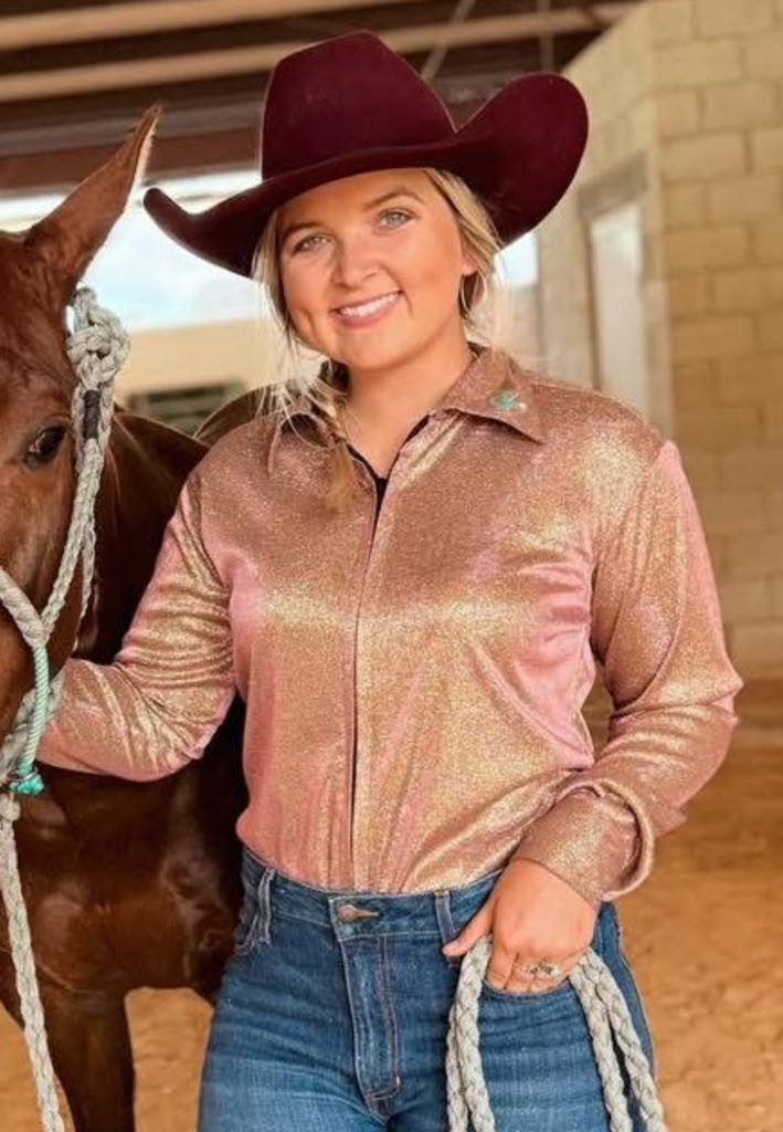 Woman wearing a metallic shimmer long sleeve shirt in a unique gold-red-rust color, standing beside a horse in a Western setting.